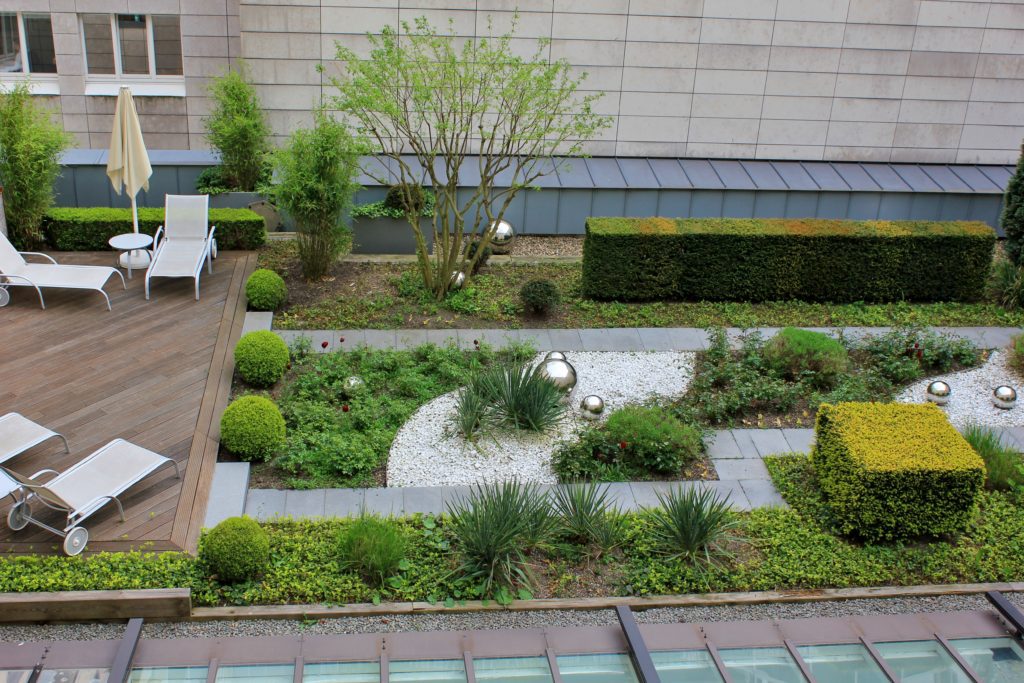 Roof garden with green plants and silver which balls and wooden terrace with rest chairs